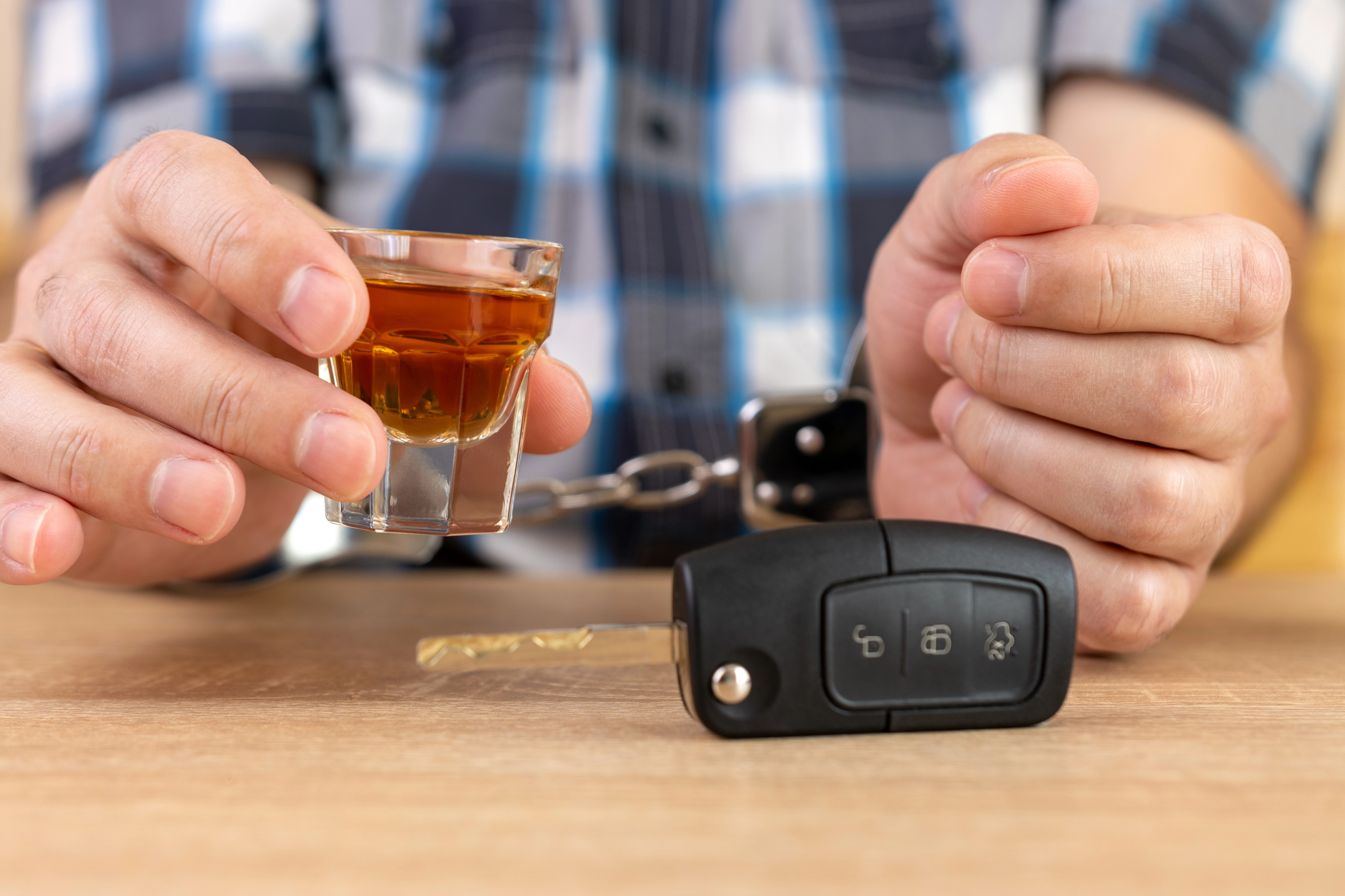 Close-up of a driver in handcuffs with a shot of liquor and car keys on the table, representing the consequences of a DWI arrest in New York.